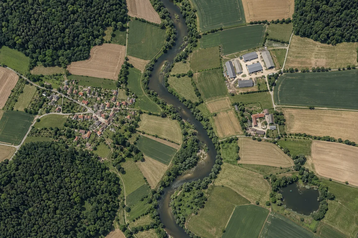 A fictional aerial landscape with a winding river, forests, fields, and a small village.